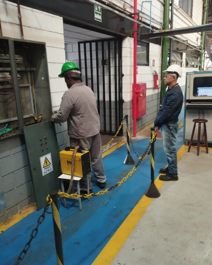 Dois técnicos da JW de capacete trabalhando em painel elétrico industrial, com a área isolada