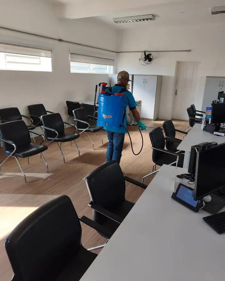 Técnico da JW com pulverizador costal e luvas aplicando produto em escritório